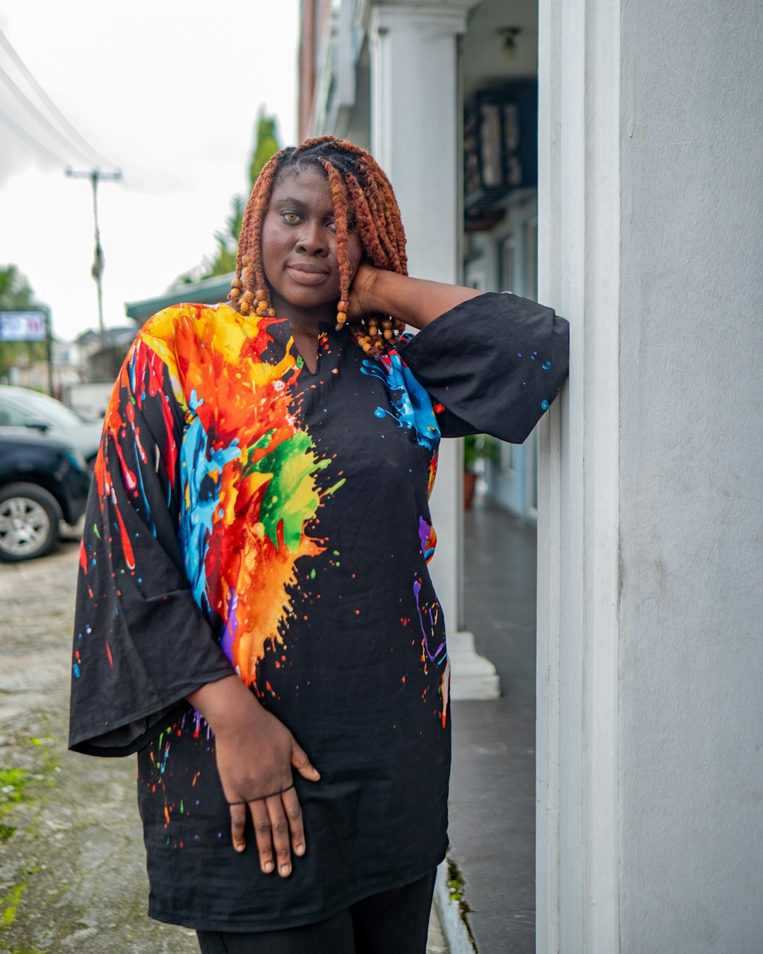 woman-in-colorful-paint-splatter-shirt-leans-on-column-lirxpg3sqem